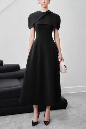 Woman wearing a black dress with a draped neckline in a minimalistic setting.